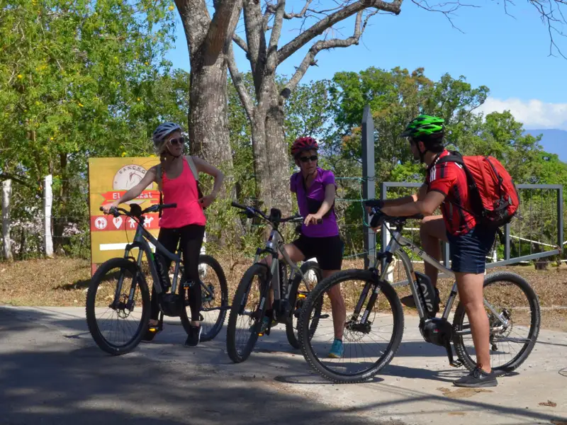 Drei Radfahrer machen eine Pause an einem Wegweiser während ihrer Radtour.