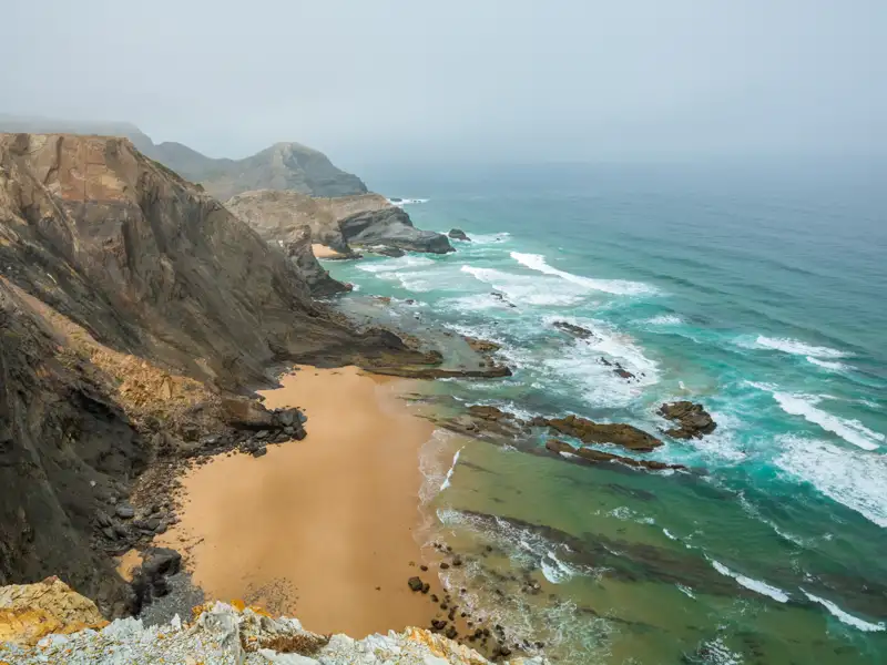 Steile Klippen und ein Sandstrand treffen auf das türkisfarbene Meer.