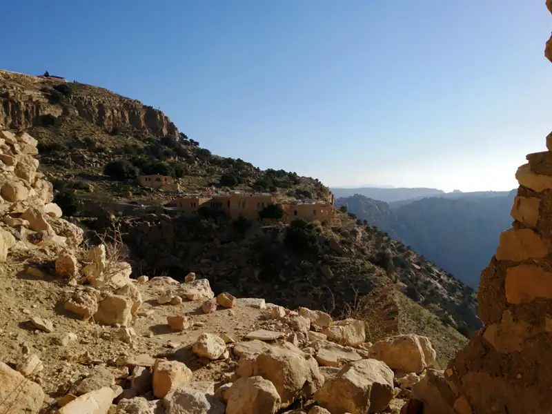 Blick durch eine Steinmauer auf ein Bergdorf in einer felsigen Berglandschaft.