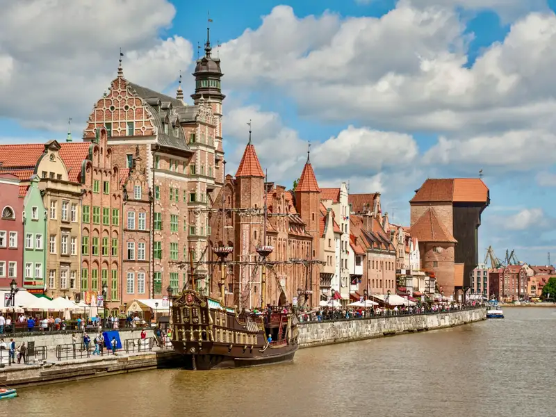 Blick auf die historische Architektur der Danziger Altstadt, darunter das Krantor und ein im Hafen liegendes Schiff.