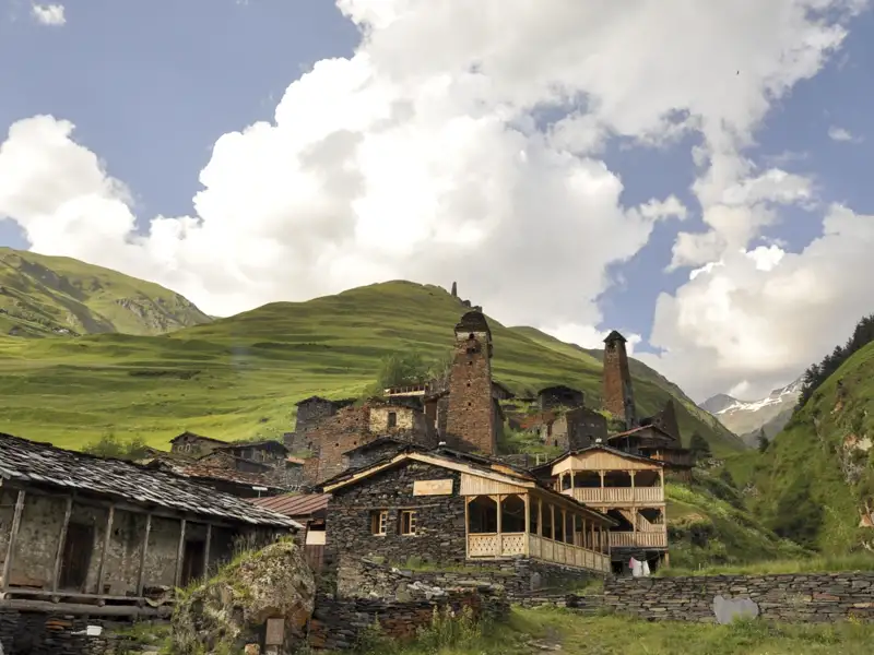 Historische Architektur eines Bergdorfes mit traditionellen Steinhäusern und Wehrtürmen inmitten einer grünen Berglandschaft.