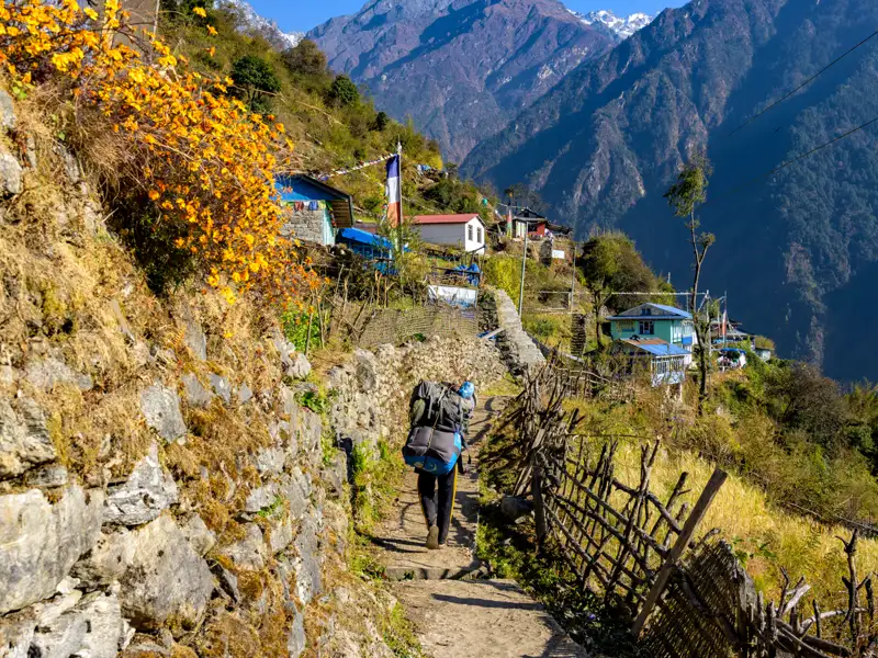 Wanderer auf einem Bergpfad in Nepal, umgeben von Bergdörfern und der beeindruckenden Kulisse des Himalayas.