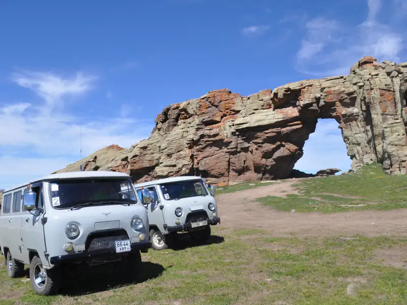 Reisebusse am Fuße eines Felsentors, welches Teil einer natürlichen Felsformation ist.
