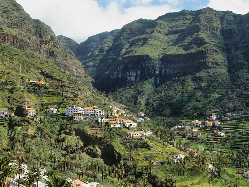 Blick auf ein Dorf in einem Tal mit Terrassenfeldern und umliegenden Bergen.