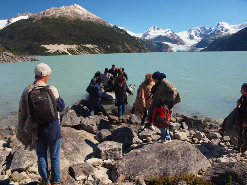 Touristen beim Ausstieg aus einem Boot an einem Gletschersee, umgeben von schneebedeckten Bergen.