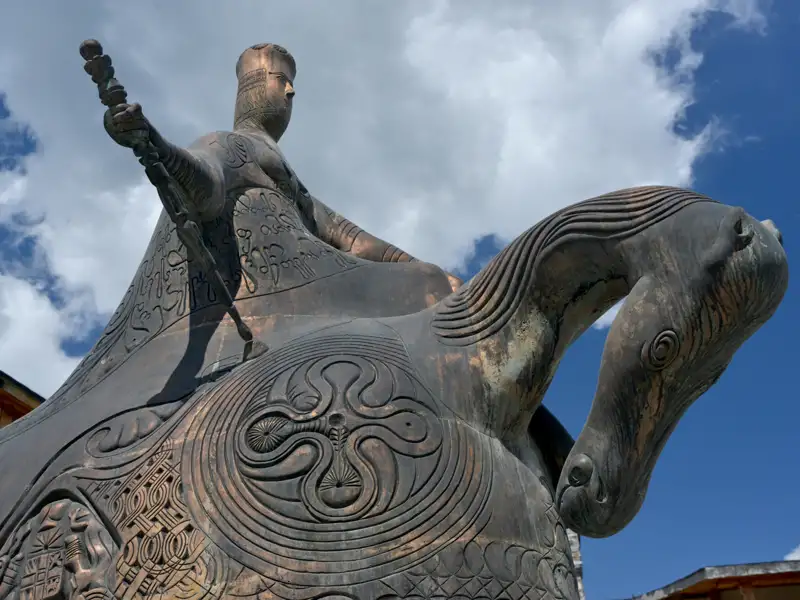 Wanderer auf einem Bergpfad inmitten blühender Vegetation mit Blick auf die Berglandschaft.