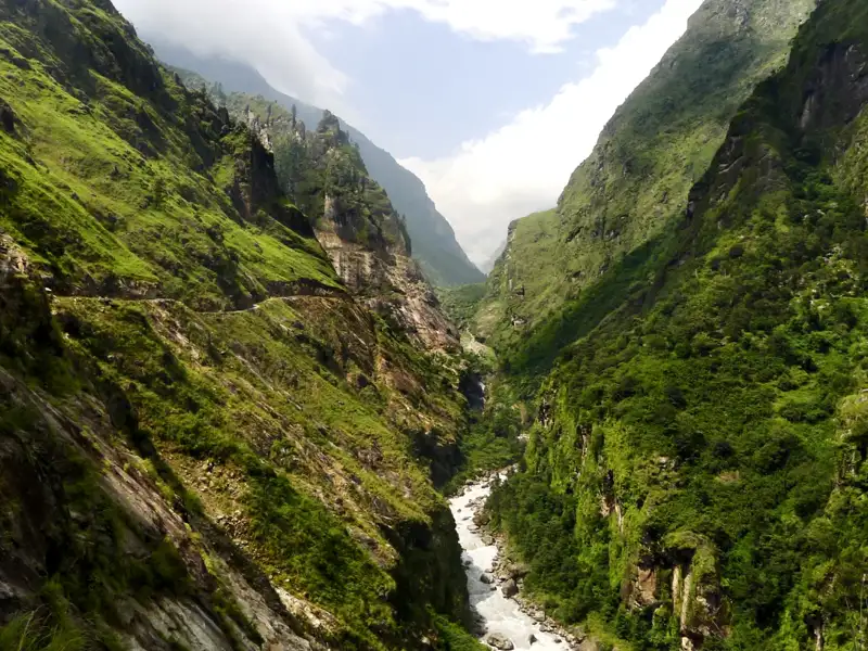 Ein Bergpfad in einem üppigen Tal mit einem Flusslauf.