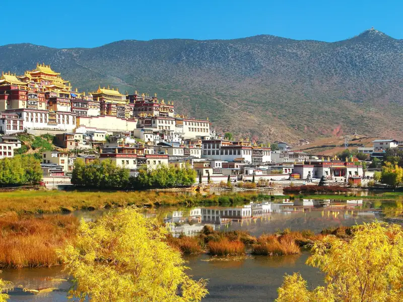 Herbstliche Ansicht eines Bergklosters mit See im Vordergrund.