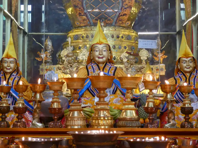 Drei goldene Mönchsstatuen mit Opfergaben und brennenden Öllampen.