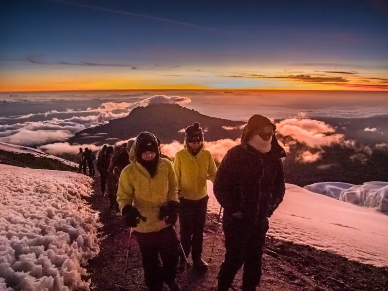 Wanderer besteigen einen verschneiten Bergpfad bei Sonnenaufgang.
