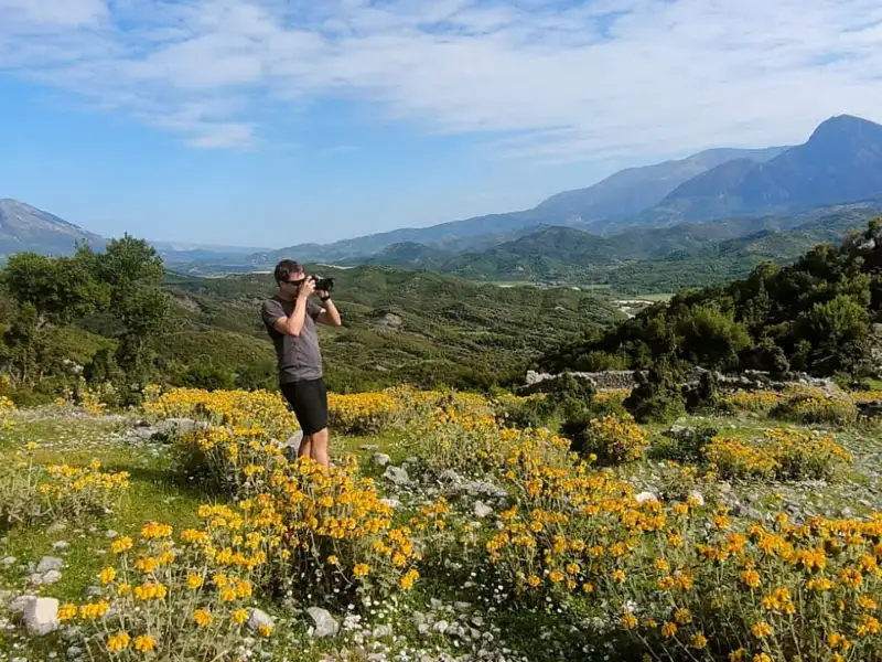 Reisender fotografiert eine Berglandschaft mit gelben Wildblumen.
