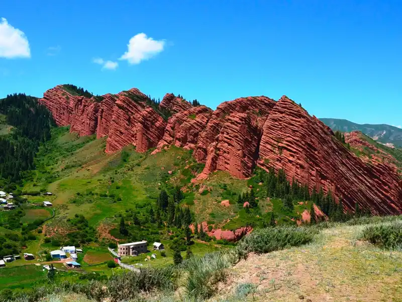 Spektakuläre rote Felsformationen, die sich über eine grüne Landschaft erstrecken.