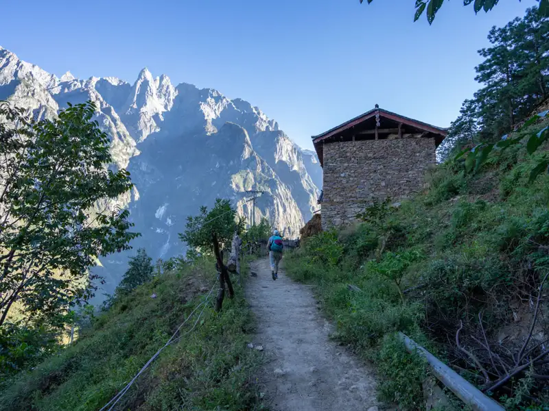Wanderung auf einem Bergpfad mit Blick auf ein Steinhaus und schneebedeckte Berge.
