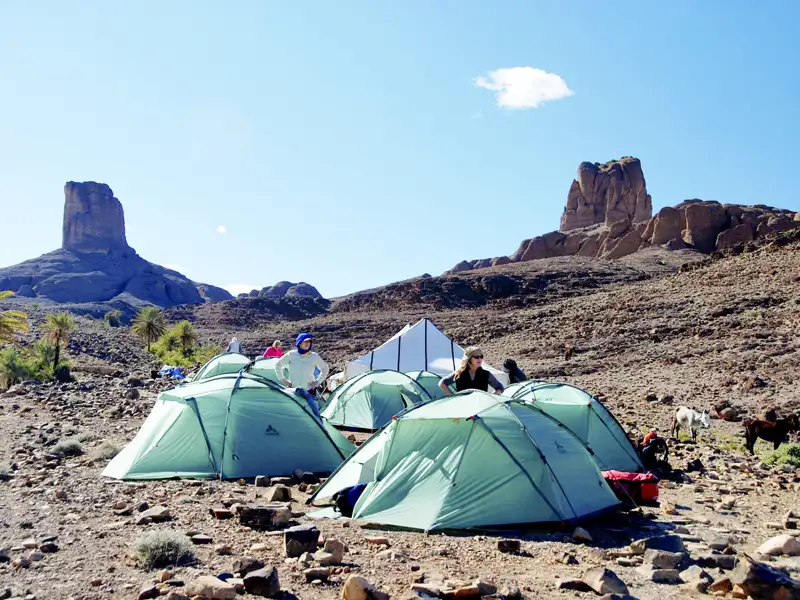 Campingplatz in der Wüste mit Zelten und Felsformationen im Hintergrund.