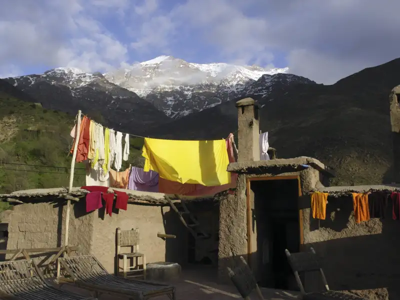 Traditionelles Lehmhaus mit Wäscheleine und schneebedeckten Bergen im Hintergrund.