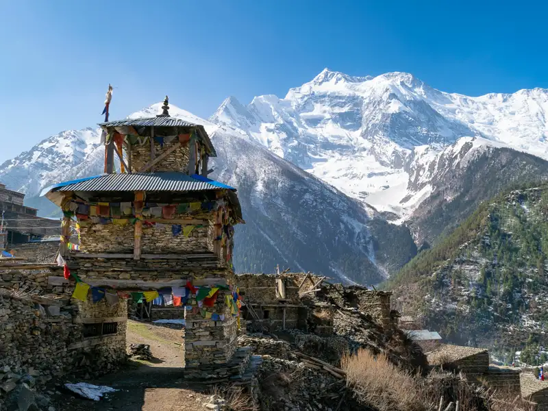 Traditioneller Steinbogen mit Gebetsfahnen und Blick auf die schneebedeckten Berge des Himalaya.