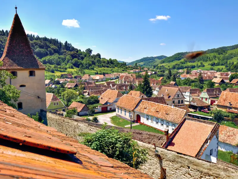 Blick auf ein traditionelles Dorf mit roten Ziegeldächern und einem Kirchturm.