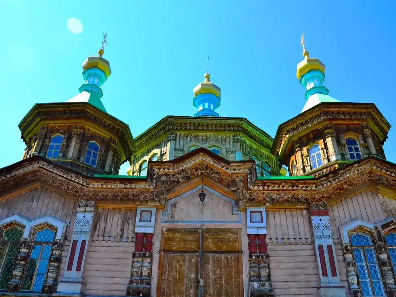 Fassade einer Holzkirche mit detaillierten Schnitzereien und grün-goldenen Kuppeln.