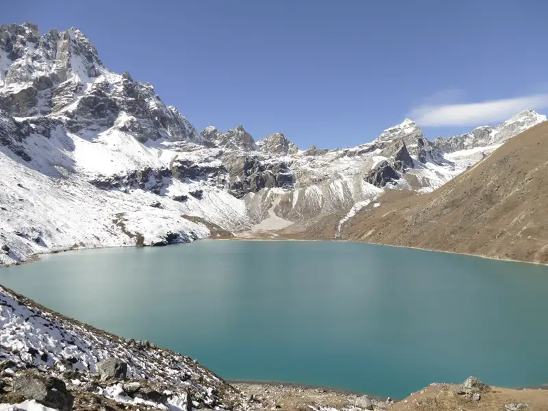 Türkisfarbener Bergsee umgeben von schneebedeckten Gipfeln.