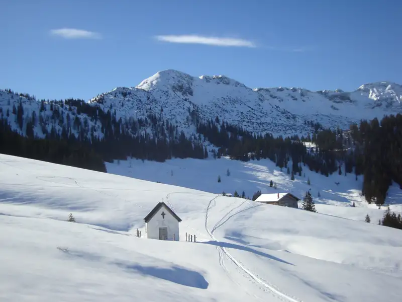 Verschneite Berglandschaft mit Kapelle und Hütte.