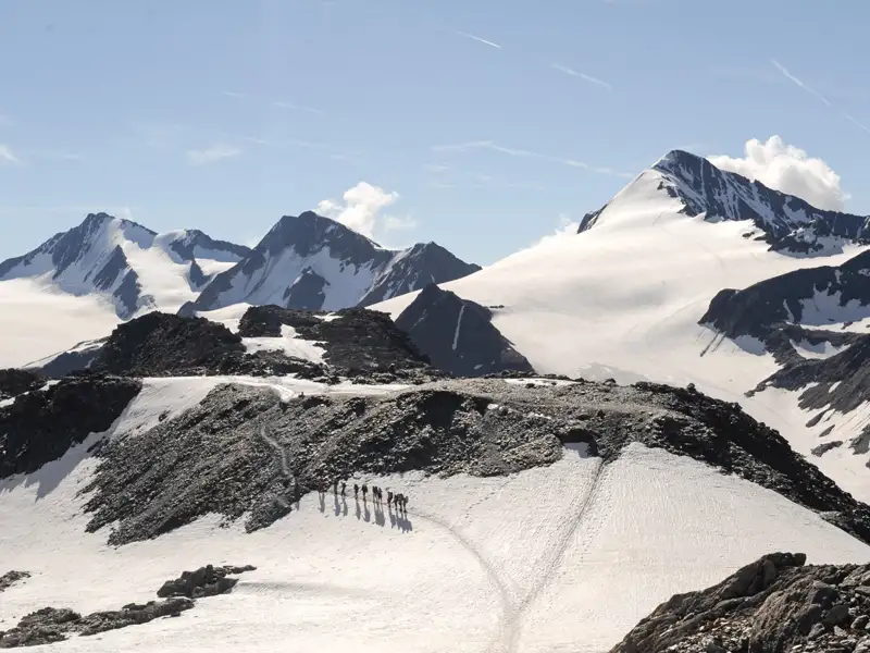 Wandergruppe auf einem schneebedeckten Bergpfad mit Gletscher im Hintergrund.