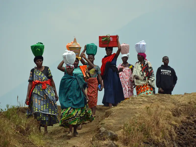 Frauen tragen Güter auf ihren Köpfen, möglicherweise auf einer Reise oder einem Transportweg.