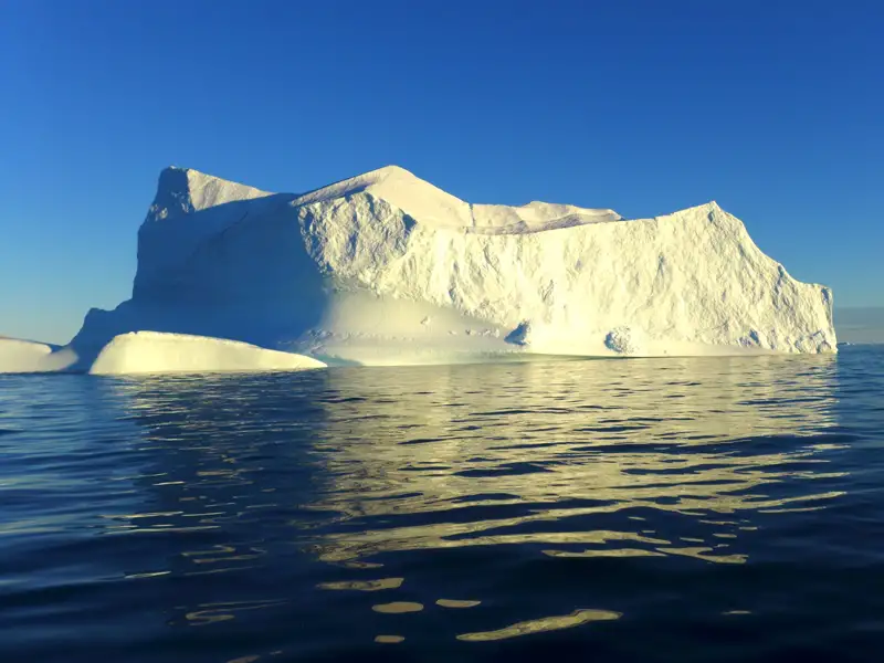 Wanderer auf einem Felsen mit Blick auf zahlreiche Eisberge im Meer.