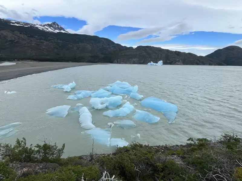 Eisberge treiben im See vor einer Bergkulisse.