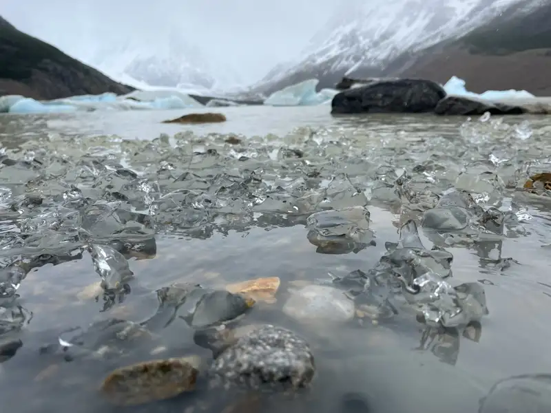 Eisschollen und Steine im Vordergrund, Gletscher und Berge im Hintergrund.