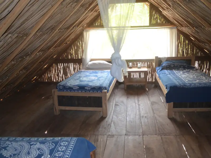 Zwei Einzelbetten in einem Zimmer mit Dachschrägen aus Bambus und Moskitonetz.