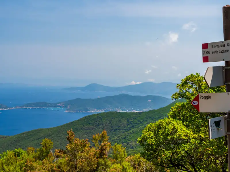 Wegweiser an einem Wanderweg mit Aussicht auf die Küste und das Meer.