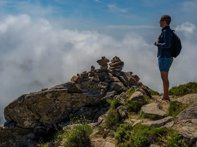 Wanderer auf einem Berggipfel mit Blick auf die Wolken.