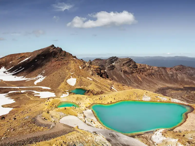 Türkisfarbene Bergseen in einer vulkanischen Landschaft mit Schneefeldern.