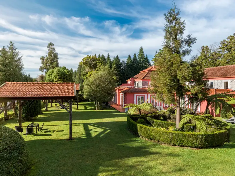 Das Hotel bietet einen gepflegten Garten mit Sitzgelegenheiten und Blick auf das rot gestrichene Hauptgebäude.