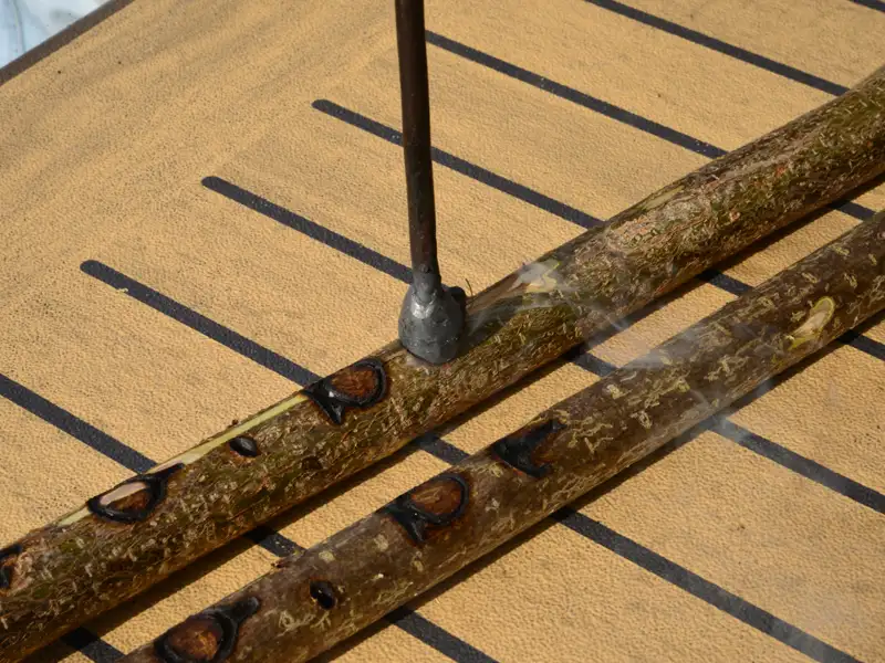 Heißes Eisen brennt Löcher in Holzstöcke, Rauchentwicklung sichtbar.