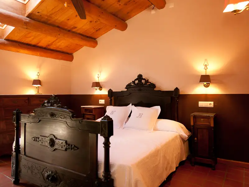 Antikes Bett im gemütlichen Schlafzimmer mit Holzbalkendecke.