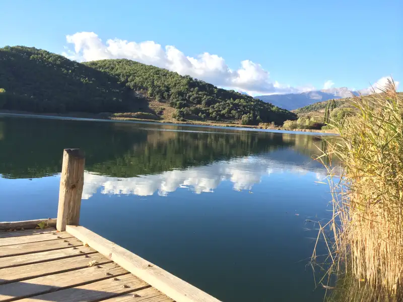 Holzsteg am See mit Blick auf Hügel und Himmel.
