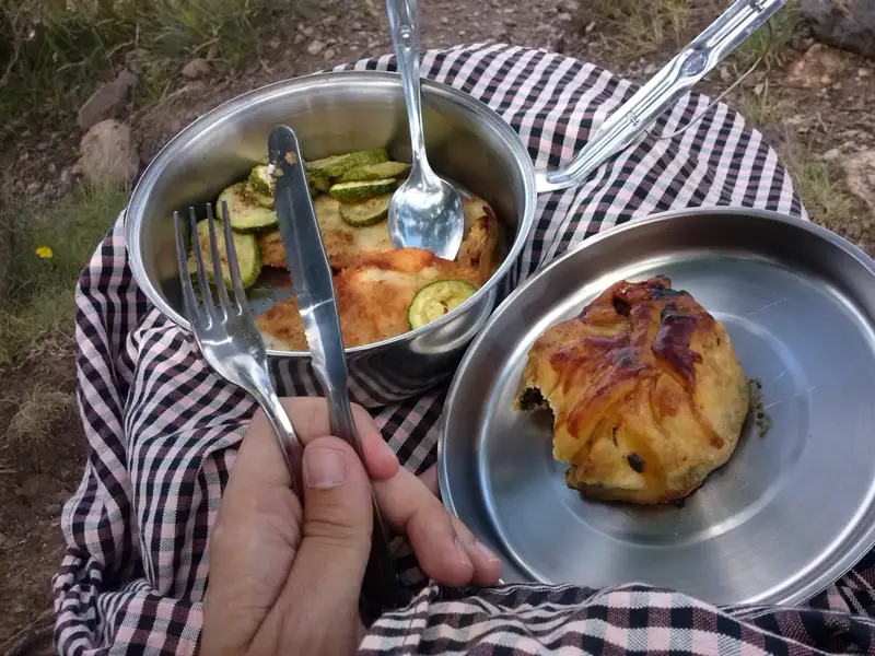 Essen während der Reisepause: Gebratenes Fleisch mit Zucchini und Gebäck in Metallbehältern.
