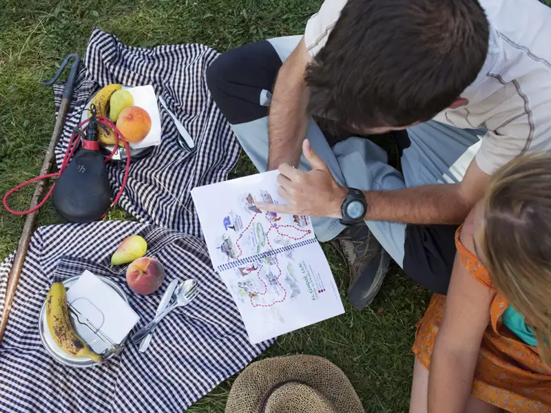Wanderer betrachten eine Wanderkarte und planen den weiteren Verlauf ihrer Route. Neben ihnen liegen Proviant und Ausrüstung.