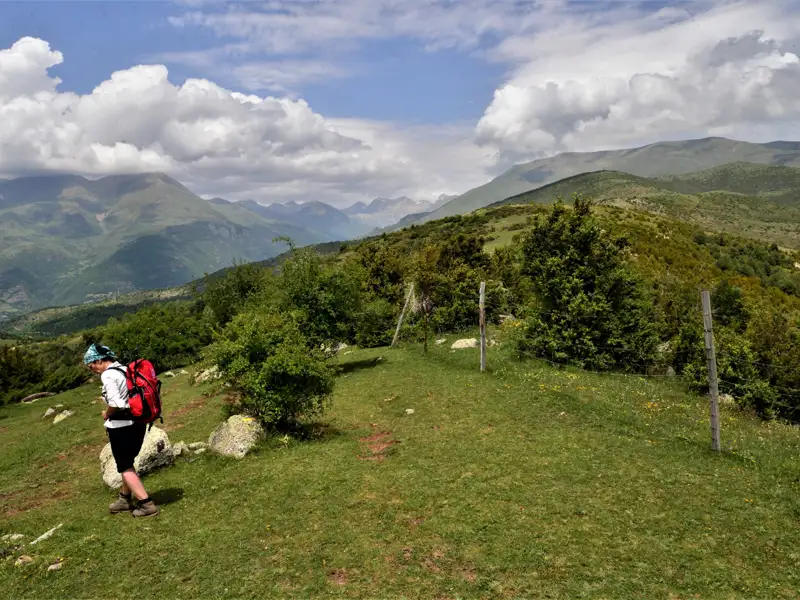 Wanderer mit rotem Rucksack auf einem Bergpfad mit Blick auf eine Berglandschaft.