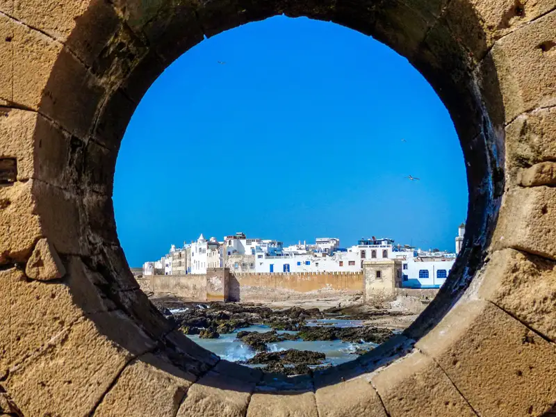 Blick auf die Küstenstadt durch ein rundes Fenster in der Stadtmauer.