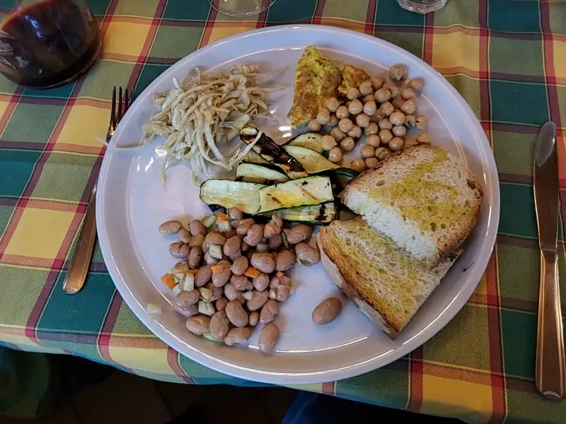 Teller mit verschiedenen Speisen: Gegrillte Zucchini, Bohnensalat, Kichererbsen, Omelett, geriebenes Gemüse und Brot.