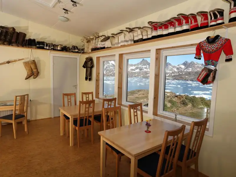 Blick aus dem Restaurant auf die Eisberge und die umliegende Landschaft. Traditionelle grönländische Kleidung und Schuhe sind Teil der Dekoration.
