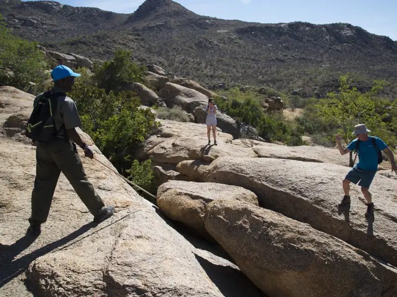 Wanderer beim Überqueren von Felsen in bergigem Gelände mit Hilfe eines Seils.