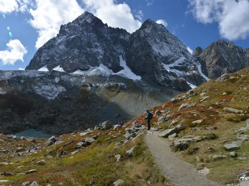 Wanderweg in den Alpen mit schneebedeckten Gipfeln im Hintergrund.