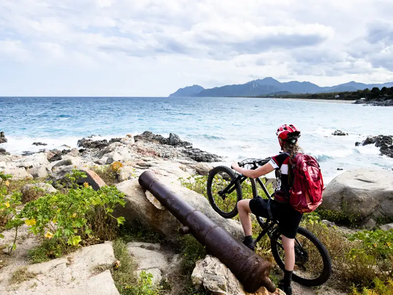 Mountainbikerin macht Pause an der Küste neben einer alten Kanone und genießt den Blick auf das Meer.
