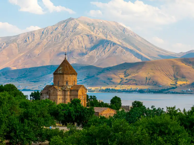 Historische Kirche am Ufer eines Sees mit imposanter Bergkulisse.