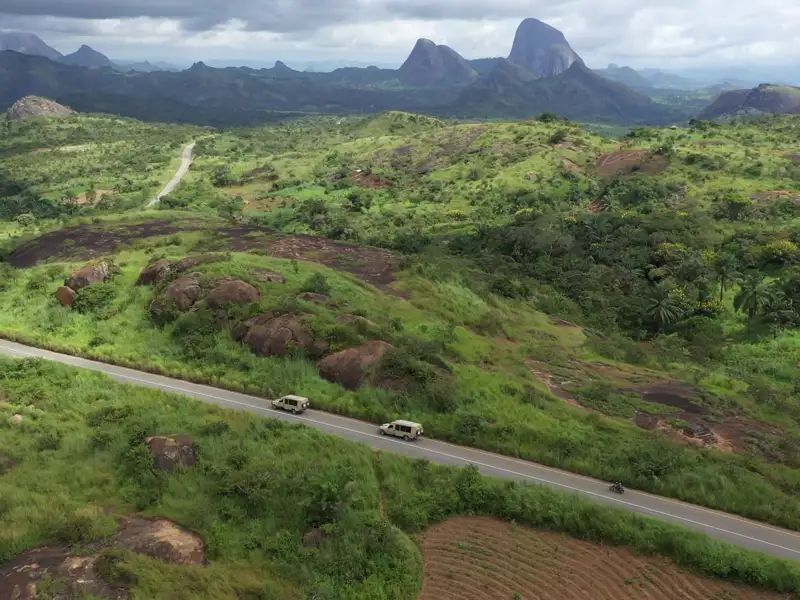 Zwei Fahrzeuge auf einer Reise durch eine hügelige Landschaft mit Felsformationen im Hintergrund.
