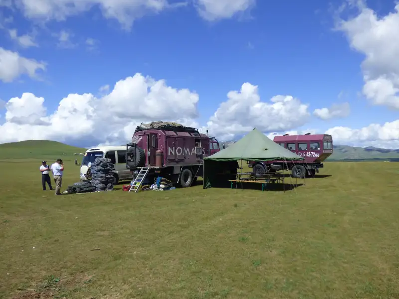 Reisecamp mit Fahrzeugen und Zelt auf einer Wiese.