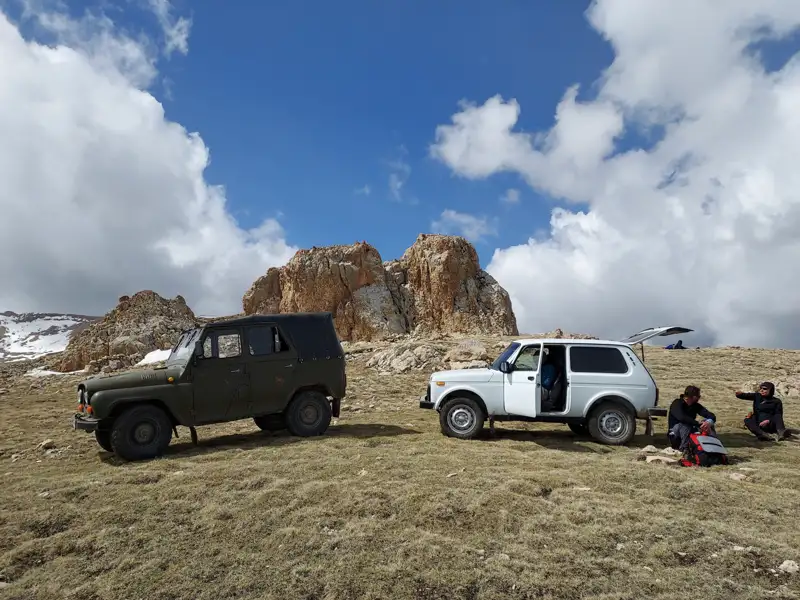 Geländewagen als Transportmittel in den Bergen. Reisende ruhen sich neben den Fahrzeugen aus.